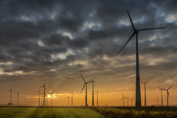 Many wind turbines on a field in northern Germany. Despite the sunset, many dark clouds are in the sky and convey a disturbing mood.