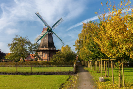 A park in the sunshine in the small town of Jemgum near Emden in northern Germany. Beautiful trees, greenery and a windmill can be seen.