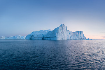 Fototapeta na wymiar Photogenic and intricate iceberg under an interesting and blue sky during sunset. Effect of global warming in nature. Conceptual image of melting glacier in deep blue water in Antarctica or Greenland
