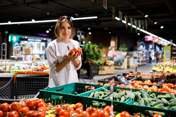 Young pretty girl is shopping in a big store. The girl buys groceries at the supermarket. Girl chooses fresh vegetables