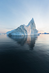 Fototapeta na wymiar Photogenic and intricate iceberg under an interesting and blue sky during sunset. Effect of global warming in nature. Conceptual image of melting glacier in deep blue water in Antarctica or Greenland
