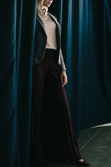 cropped view of elegant woman in palazzo pants standing near curtain