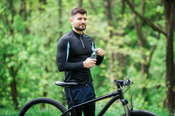 Tired biker resting and drinking from water bottle in green park