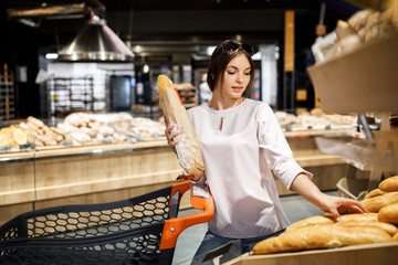 Young pretty girl is shopping in a big store. The girl buys groceries at the supermarket. The girl chooses a fragrant pastry