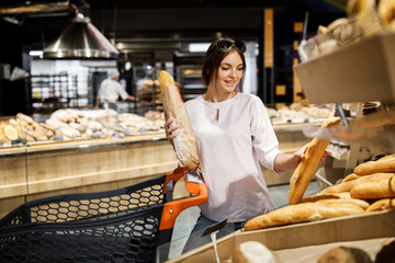 Young pretty girl is shopping in a big store. The girl buys groceries at the supermarket. The girl chooses a fragrant pastry