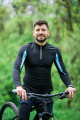 Young bright man on mountain bike in green forest