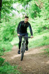 Handsome young man biking in the countryside in green forest