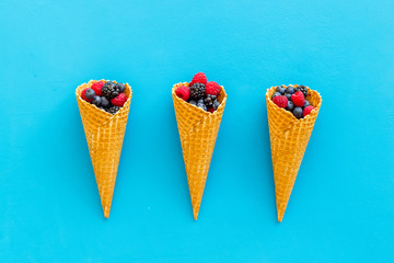 Summer breakfast with fresh berries in waffle cones on blue background top view