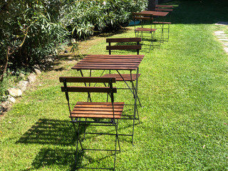 Wooden chairs and tables on green grass in park 