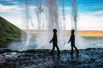 two girls walking under a waterfall - obrazy, fototapety, plakaty