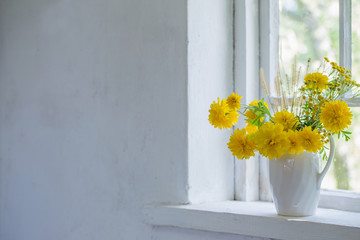 yellow flowers in white jug on windowsill
