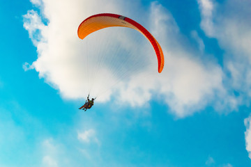 Orange paraglide flying on a cloudy sky