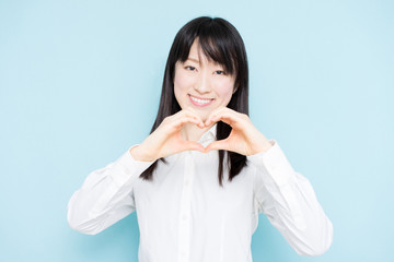 Young business woman showing heart gesture against light blue backgournd