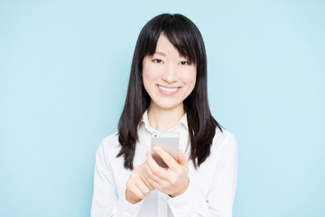 Young business woman holding smart phone against light blue background