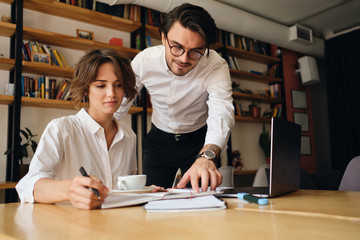 Young attractive business colleagues dreamily working on new project with laptop in office