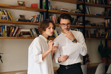 Young pensive business colleagues standing with papers thoughtfully discussing work together in office