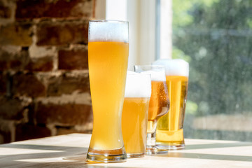 Glasses of different kinds of light beer in sunlight on brick wall background. Cold delicious alcohol drinks are prepared for a big friend's party. Concept of holiday, fun, meeting, oktoberfest.