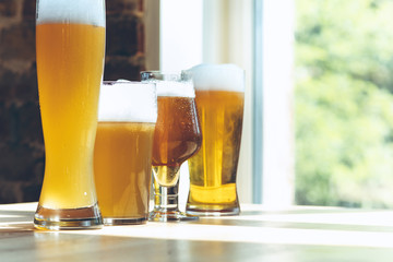 Glasses of different kinds of light beer in sunlight on brick wall background. Cold delicious alcohol drinks are prepared for a big friend's party. Concept of holiday, fun, meeting, oktoberfest.