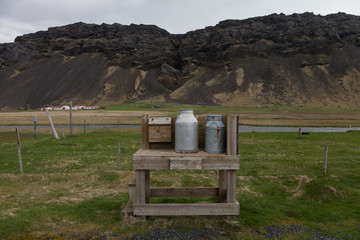 Metal farm cans on a wooden bench on a beautiful multicolored spring landscape of Iceland
