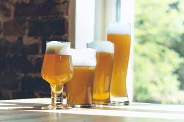 Glasses of different kinds of light beer in sunlight on brick wall background. Cold delicious alcohol drinks are prepared for a big friend's party. Concept of holiday, fun, meeting, oktoberfest.