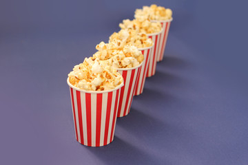 flavored crispy popcorn poured into five striped white-red paper glasses that stand in a row behind each other on a lilac background, copy space
