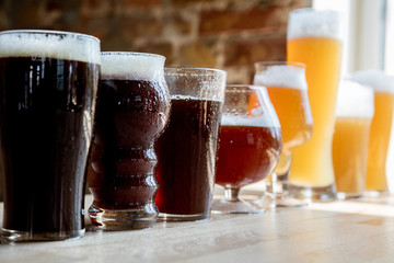 Glasses of dark and light beer and ale in sunlight on brick wall background. Cold delicious alcohol drinks are prepared for a big friend's party. Concept of holiday, fun, meeting, oktoberfest.