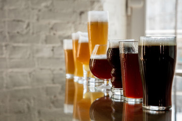 Glasses of dark and light beer and ale in sunlight on brick wall background. Cold delicious alcohol drinks are prepared for a big friend's party. Concept of holiday, fun, meeting, oktoberfest.
