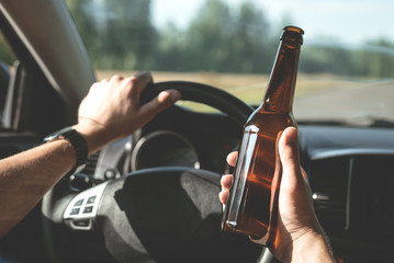 Driver is driving a car with a bottle of beer in hand. Drunk driving concept.
