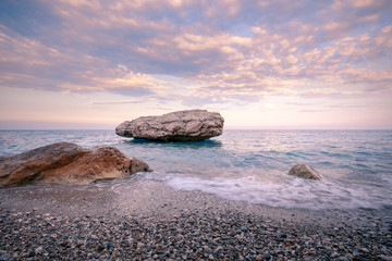 Summer beach coast with textured rocks and pebbles, covering with wave.