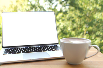 Fototapeta premium Mock up image of a pleasant morning using a laptop with a blank white desktop screen with a cup of coffee on a wooden table in an outdoor cafe