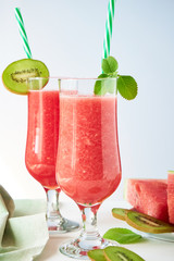 Two glasses of fresh watermelon smoothie with kiwi and mint on a white wooden table