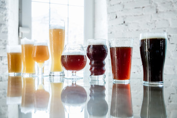 Glasses of dark and light beer and ale in sunlight on brick wall background. Cold delicious alcohol drinks are prepared for a big friend's party. Concept of holiday, fun, meeting, oktoberfest.