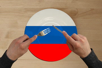 hands with cutlery on a plate with the state national flag of Russia, copy space