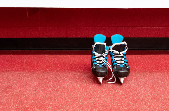 Kids hockey skates over floor and red background in locker room with copy space