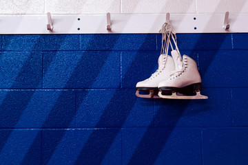 Figure skates hanging over gradient blue wall in locker room with copy space