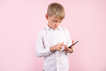 sad schoolboy got bad news sms from mom or friends. dressed in a white shirt and standing in front of a pink background