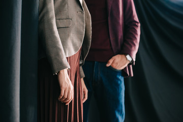 cropped view of stylish young woman and man standing with hand in pocket near curtain