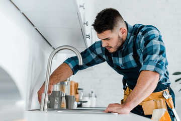 selective focus of handsome handyman working near sink in kitchen