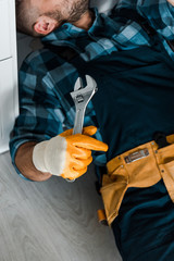 cropped view of bearded worker holding adjustable wrench while working in kitchen