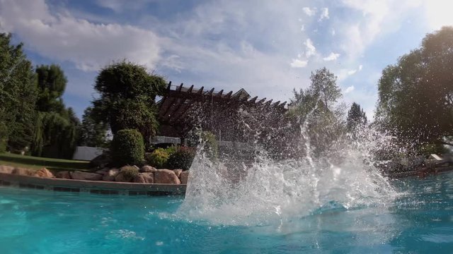 Side view of young man doing a gainer into a swimming pool.