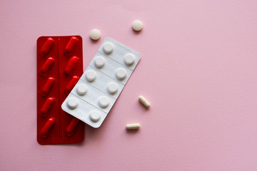 Medicine capsules and tablets  in red and white blister packs on a pink background. Isolated. Copy space.