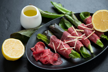 Rolls with carpaccio beef, salad leaves and parmesan cheese served on a black plate, studio shot
