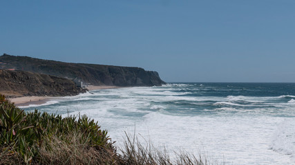 Fototapeta na wymiar Cliff top view of Praia Grande from Praia das Maçãs, Portugal & the waves of the Atlantic ocean. Taken on a sunny summer day.