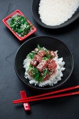 Poke bowl with tuna fillet over black stone background, vertical shot