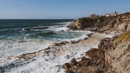 View of cliff top villas and the Atlantic ocean waves on a sunny summer day, taken in Praia das Maçãs, Sintra, Portugal