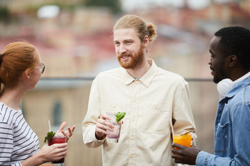 Group of young people talking to each other and drinking cocktails while standing at party outdoors