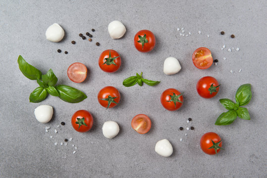 Fresh cherry tomatoes with basil leaves, mini mozzarella and black pepper on a stone table, vegetable pattern, top view