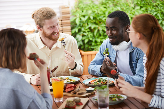 Group of friends talking and smiling to each other while eating meal at lunch at the restaurant