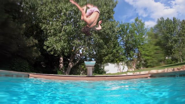 Teenage boy running and doing a backfilp gainer into a pool on hot summers day.