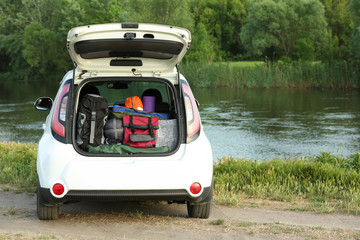 Car with camping equipment in trunk on riverbank. Space for text © New Africa